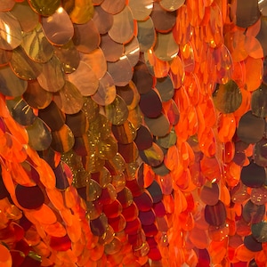 May include: Orange iridescent sequins on a mesh fabric. The sequins are arranged in a scale-like pattern.