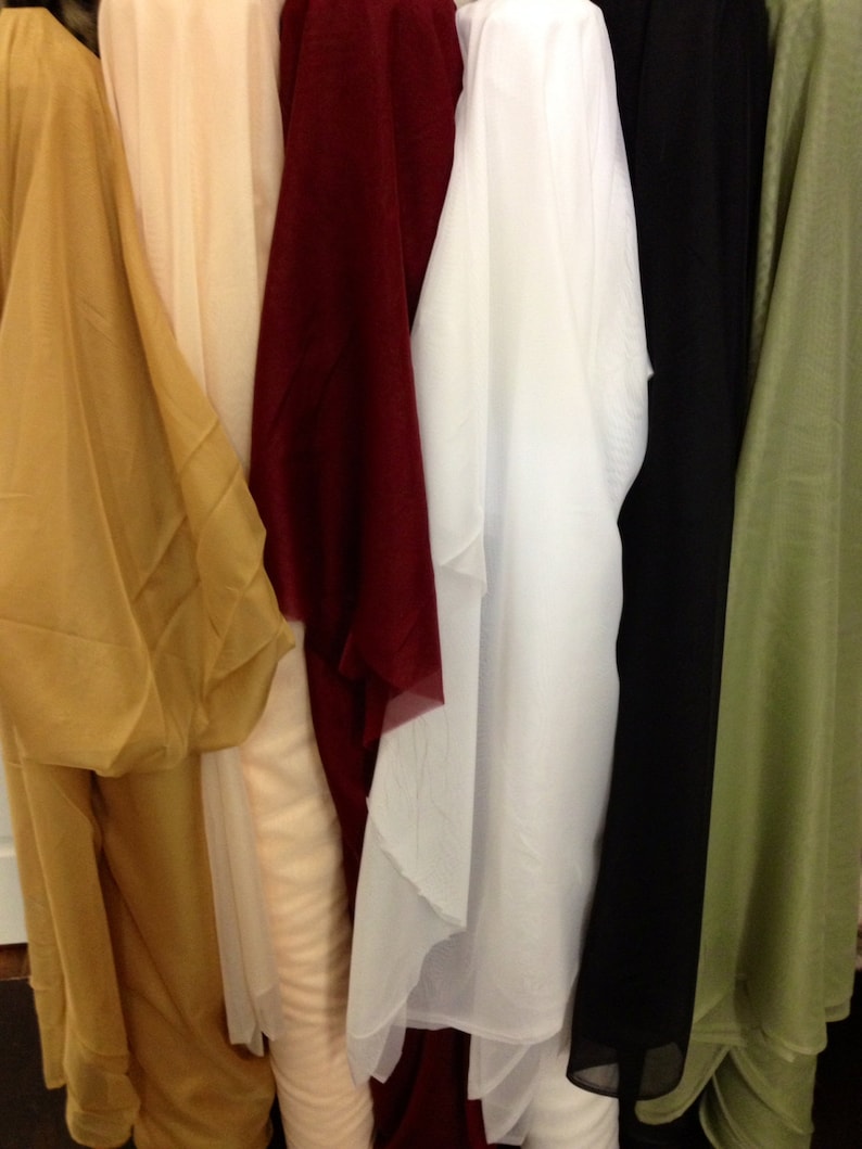 May include: A display of fabric rolls in a range of colours: gold, cream, burgundy, white, black, and olive green. The fabrics look lightweight and flowing, ideal for clothing or decorative use.
