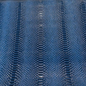 May include: A close-up of a textured, navy blue surface with a pattern resembling snake or reptile skin. The pattern is made up of small, overlapping scales, creating a glossy, reflective appearance. The scales are arranged in vertical rows.