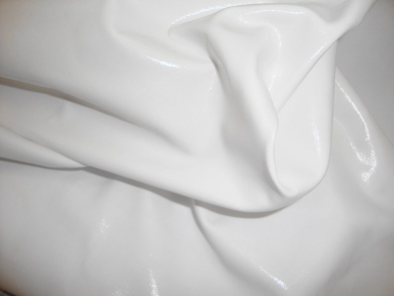 Peut inclure: Un morceau de tissu vinyle blanc avec une finition brillante et r&eacute;fl&eacute;chissante. Le mat&eacute;riau est drap&eacute; pour cr&eacute;er des plis doux et fluides ainsi que des ombres profondes, soulignant la texture lisse et la couleur blanche unie &eacute;clatante.