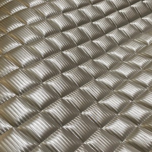 May include: A close-up of a silver quilted fabric with a diamond pattern. The fabric has a subtle sheen and a textured surface.