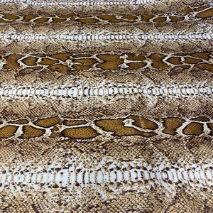May include: A close-up of a snakeskin pattern. The pattern features a mix of brown, tan, and white scales, creating a realistic reptile skin texture. The design is arranged in horizontal bands.