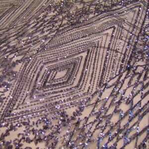 May include: Purple iridescent sequins are sewn in a geometric pattern on a sheer mesh fabric. The sequins create a diamond shape design.