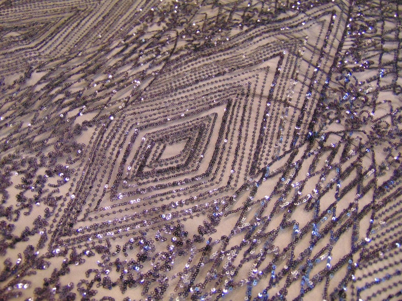 May include: Purple iridescent sequins are sewn in a geometric pattern on a sheer mesh fabric. The sequins create a diamond shape design.