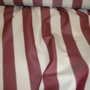 May include: Red and white striped fabric with a subtle sheen. The fabric is folded and draped, showing the texture and pattern.
