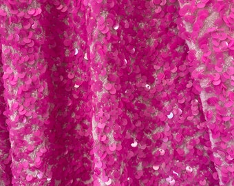 May include: Close-up of a pink fabric with sequins. The sequins are arranged in a pattern and create a shimmering effect.