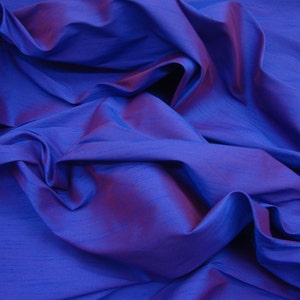 May include: A close-up of a deep blue fabric with a subtle iridescent sheen. The fabric is draped and folded, creating soft, flowing lines.