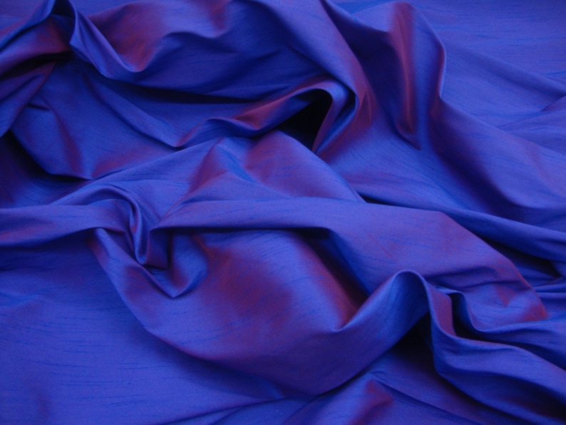 May include: A close-up of a deep blue fabric with a subtle iridescent sheen. The fabric is draped and folded, creating soft, flowing lines.