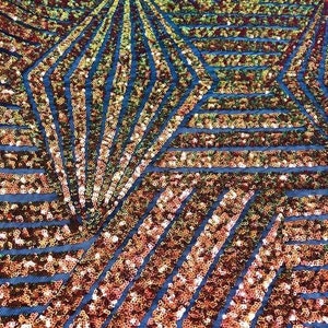 May include: Close-up of a shimmering fabric with a geometric pattern. The fabric features a blue mesh base covered in bronze and gold sequins arranged in a repeating diamond and stripe design. The sequins catch the light, creating a sparkling effect.