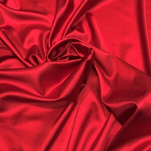 May include: A close-up of a smooth, red satin fabric with a soft, luxurious texture. The fabric is draped and folded, creating a dramatic and elegant look.