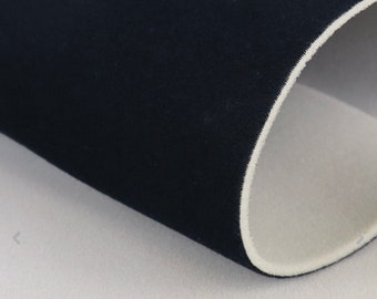 May include: Close-up of a rolled piece of black fabric with a white interior. The fabric appears to be a soft, textured material, possibly neoprene or a similar textile. The edges are neatly finished.