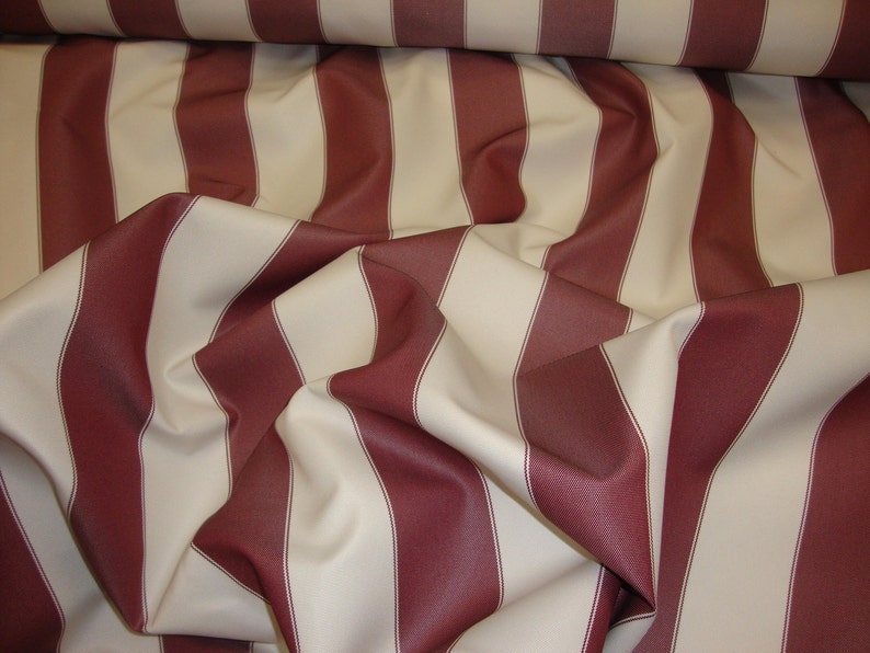 May include: Red and cream striped fabric with a woven texture. The fabric is folded and draped, showing the stripes.