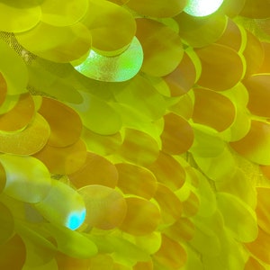 May include: Close-up of a yellow fabric with overlapping round sequins. The sequins have a slight iridescent sheen.