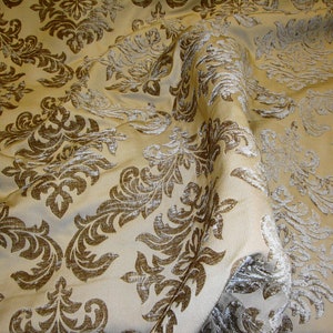 Pu&ograve; includere: Un tessuto beige con un motivo damascato marrone. Il tessuto ha una lucentezza sottile e una texture morbida.