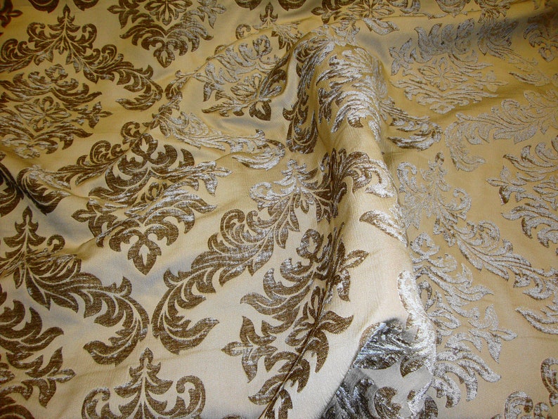 Pu&ograve; includere: Un tessuto beige con un motivo damascato marrone. Il tessuto ha una lucentezza sottile e una texture morbida.
