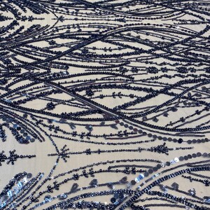 May include: Close-up of navy blue beaded fabric. The fabric is covered in intricate patterns of beads and sequins, creating a shimmering effect. The design includes lines, dots, and floral-like shapes, all in shades of navy blue.