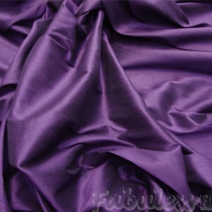 May include: A close-up of a deep purple fabric with a smooth, silky texture. The fabric is draped and folded, creating soft, flowing lines.