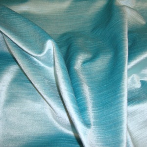 Peut inclure: Un gros plan sur un tissu bleu sarcelle avec un l&eacute;ger reflet. Le tissu est lisse et soyeux, avec une l&eacute;g&egrave;re texture. Il est drap&eacute; et pli&eacute;, cr&eacute;ant des courbes et des plis doux.