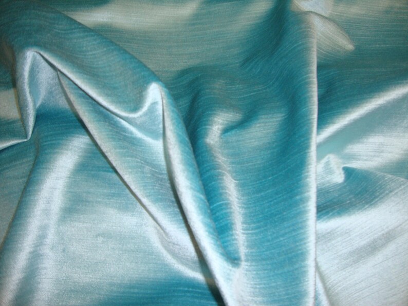 Peut inclure: Un gros plan sur un tissu bleu sarcelle avec un l&eacute;ger reflet. Le tissu est lisse et soyeux, avec une l&eacute;g&egrave;re texture. Il est drap&eacute; et pli&eacute;, cr&eacute;ant des courbes et des plis doux.