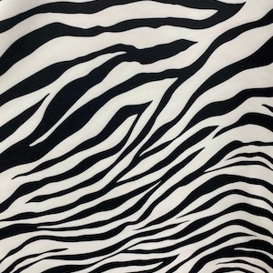 May include: Close-up of a fabric with a zebra stripe pattern. The design features bold, black stripes against a white background. The stripes are wavy and irregular, creating a dynamic and eye-catching visual texture. The fabric appears to be smooth.