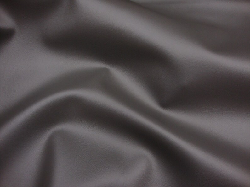 May include: A close-up of a smooth, grey fabric with a subtle texture. The fabric is draped and folded, creating soft curves and folds.