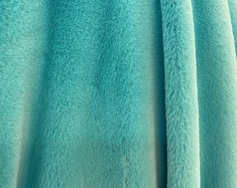 May include: A close-up of a soft, teal blue faux fur fabric. The fabric is folded and has a plush, velvety texture.