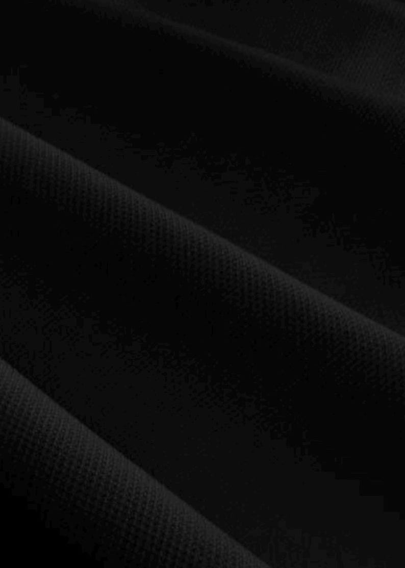 Pu&ograve; includere: Primo piano di tessuto nero con un motivo strutturato e tessuto. Il materiale &egrave; drappeggiato, creando pieghe e ombre che aggiungono profondit&agrave;. Il colore scuro suggerisce un capo di abbigliamento o un tessuto.