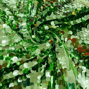 May include: A fabric covered in round, reflective green sequins. The sequins are arranged in a dense, overlapping pattern, creating a shimmering, metallic surface with varying shades of emerald and lime green visible across the texture.