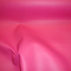 May include: A close-up of a bright pink fabric with a smooth, slightly textured surface. The fabric is folded and draped, creating soft folds and curves.