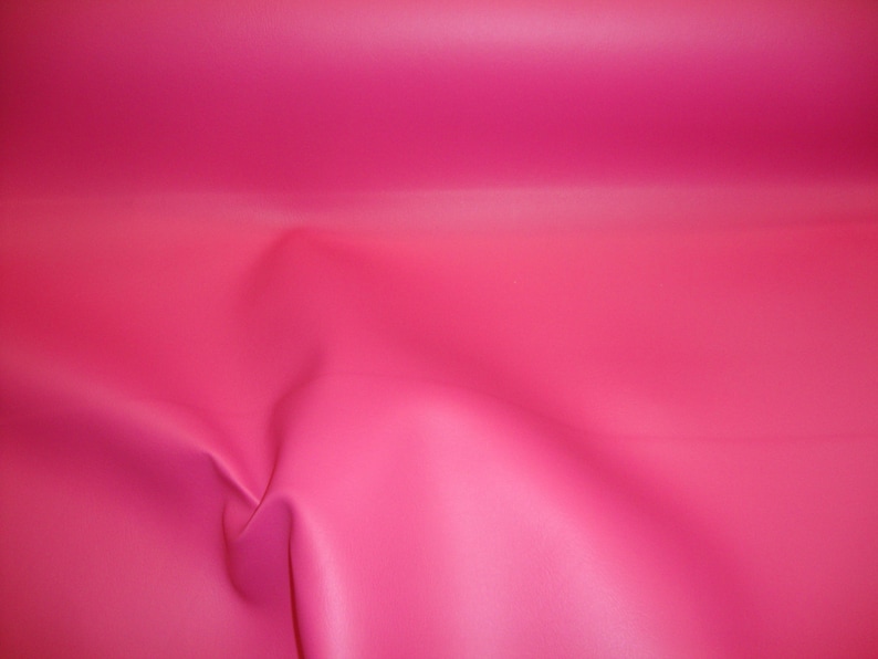 May include: A close-up of a bright pink fabric with a smooth, slightly textured surface. The fabric is folded and draped, creating soft folds and curves.