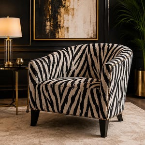May include: A barrel-style armchair upholstered in a black and white zebra print fabric. The chair features a curved backrest, a deep seat cushion, and dark wooden legs. The edges of the upholstery are accented with small metallic nailhead trim.