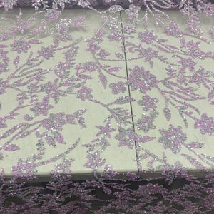 May include: A sheer fabric featuring intricate floral embroidery in light purple and silver thread. The design is densely covered with shimmering sequins that catch the light, creating a textured, sparkling pattern of interconnected vines and blossoms.