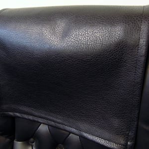 May include: Black leather headrest for a chair. The headrest is padded and has a textured surface.