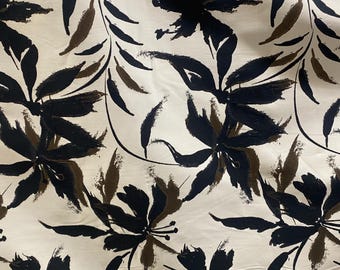 May include: White fabric with a black and brown floral print. The flowers are stylized and abstract, with long, thin petals. The background is a light cream color.