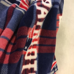 May include: A blue, red, and white fleece blanket with a plaid pattern and the word "PATRIOTS" repeated in white.