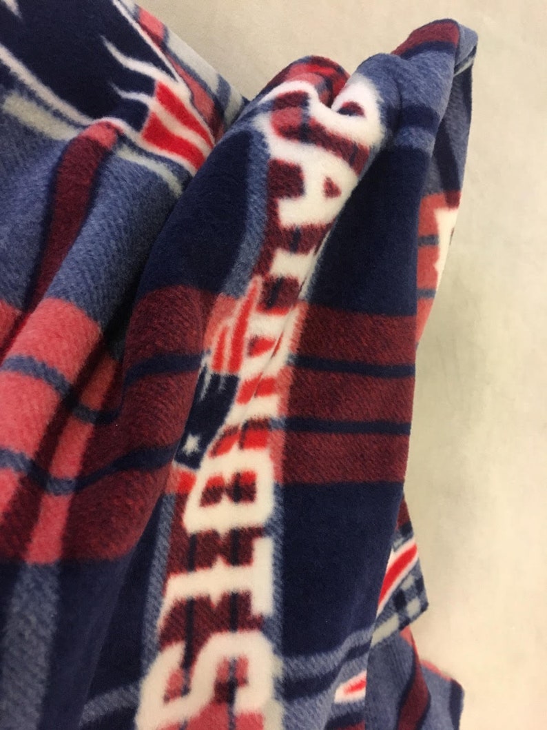 May include: A blue, red, and white fleece blanket with a plaid pattern and the word "PATRIOTS" repeated in white.