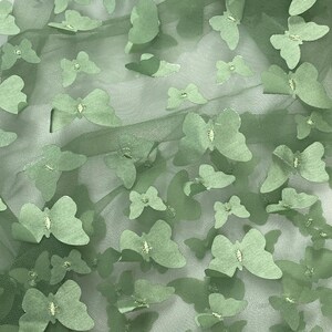 May include: Green tulle fabric with a repeating pattern of green butterfly cutouts. The fabric has a subtle shimmer.