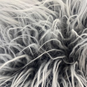 May include: Close-up of a gray and white faux fur textile. The long, shaggy fibers create a soft, textured appearance. The color palette is primarily neutral, with shades of gray and white blending together.