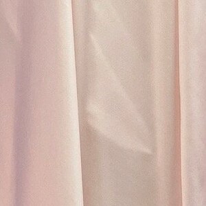 May include: A close-up of a smooth, pale pink fabric with subtle wrinkles. The fabric has a soft, silky texture.