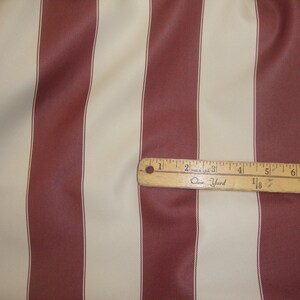 May include: Red and cream striped fabric with a wooden ruler that reads "One Yard" and has markings in inches.