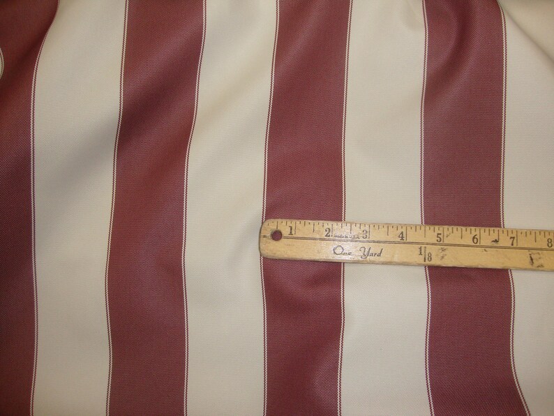 May include: Red and cream striped fabric with a wooden ruler that reads "One Yard" and has markings in inches.