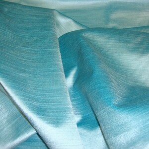 Peut inclure: Un gros plan sur un tissu bleu sarcelle avec un l&eacute;ger brillant. Le tissu est drap&eacute; et pli&eacute;, montrant sa texture et son drap&eacute;.