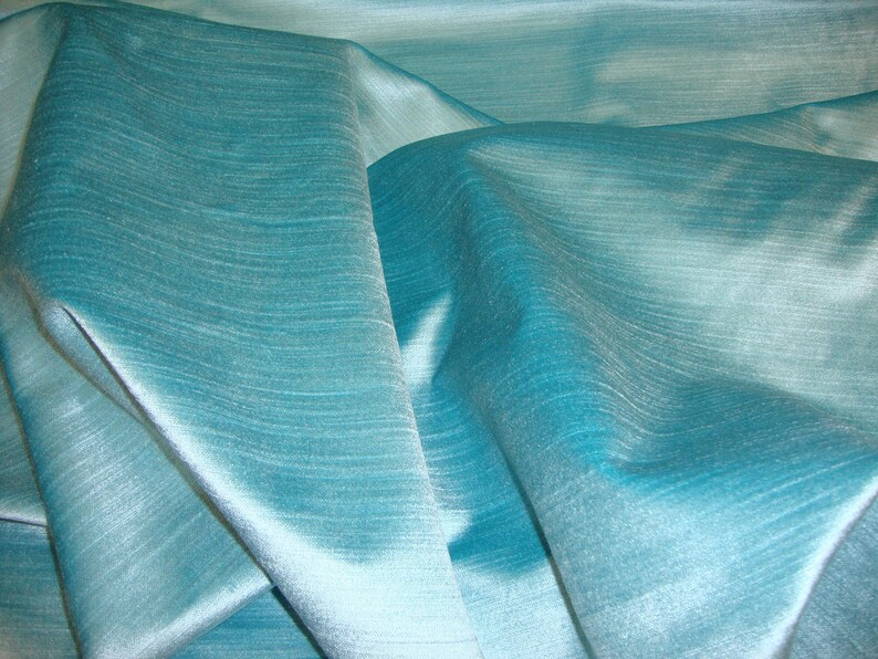 Peut inclure: Un gros plan sur un tissu bleu sarcelle avec un l&eacute;ger brillant. Le tissu est drap&eacute; et pli&eacute;, montrant sa texture et son drap&eacute;.