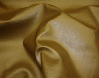 May include: A close-up of a smooth, golden brown fabric with a subtle sheen. The fabric is draped and folded, creating soft, flowing lines.