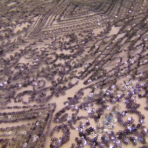 May include: A close-up of a silver sequined fabric with a geometric pattern. The sequins are small and evenly spaced, creating a shimmering effect.