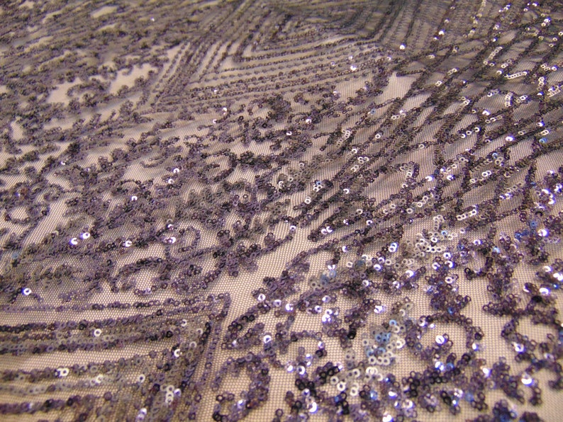 May include: A close-up of a silver sequined fabric with a geometric pattern. The sequins are small and evenly spaced, creating a shimmering effect.