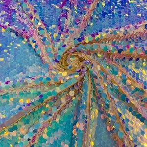 May include: A fabric covered in iridescent, circular sequins that shift in color from light blue to deep purple. The sequins are arranged in a swirling, spiral pattern that radiates outward from a central point, creating a reflective surface.