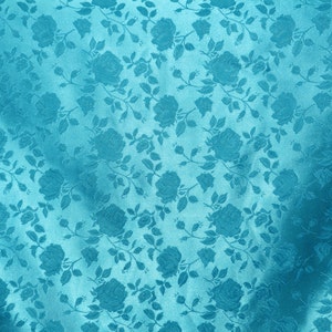May include: A teal blue fabric with a repeating floral pattern of roses and leaves.