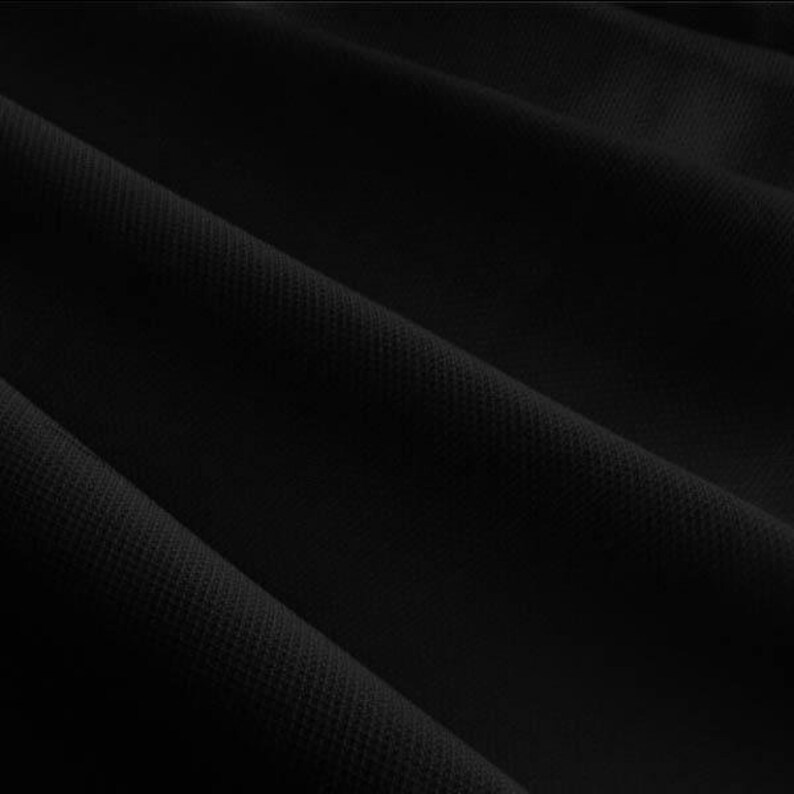 Pu&ograve; includere: Primo piano di tessuto nero con superficie strutturata. Il tessuto &egrave; drappeggiato in pieghe diagonali, creando ombre e riflessi. Il materiale sembra essere un tessuto a maglia o tessuto, adatto per abbigliamento o arredamento.