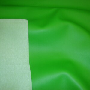 May include: A vibrant lime green fabric with a smooth, matte finish on one side and a contrasting pale, off-white felt-like backing. The material is draped to show soft folds and a flexible texture, highlighting the two distinct sides of the textile.